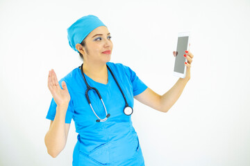 beautiful woman doctor, wearing blue uniform and blue surgical cap, stethoscope on her neck, waving at the tablet on white background