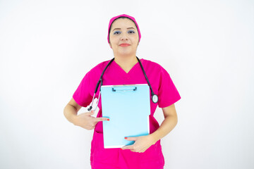 beautiful woman medical assistant, wearing uniform and pink surgical cap, stethoscope, pointing at clipboard with results, on white background