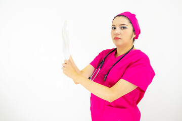 Beautiful female medical assistant wearing uniform and pink surgical cap, stethoscope, putting latex gloves, on white background