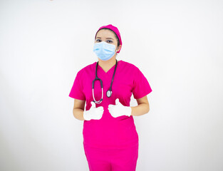 beautiful female medical assistant wearing face mask, pink uniform and pink surgical cap, latex gloves and stethoscope, on white background