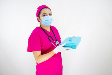 beautiful female medical assistant wearing face mask, pink uniform and pink surgical cap, stethoscope, preparing instruments case on white background