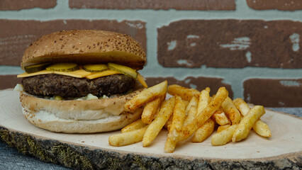 cheeseburger with cheddar chese, russian salad, pickled cucumbers, french fries on wooden tray with brick wall background