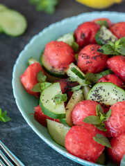 Fresh juicy watermelon-cucumber salad with mint and poppy seed in a bowl on a dark rustic table. Close-up. Selective focus. Healthy vegan plant-based diet concept.
