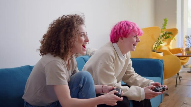 Happy young people playing video games on console while sitting on couch in front of tv. Millennial couple spending fun time together at home.Room with warm and neon lights. Gaming hobby. Friends