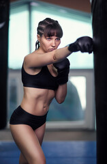 Female fighter with a boxing gloves on hands boxing on a punching bag.