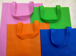 pink, green, orange, white and blue polypropylene bags. pile of tote bags of non-woven fabric with...