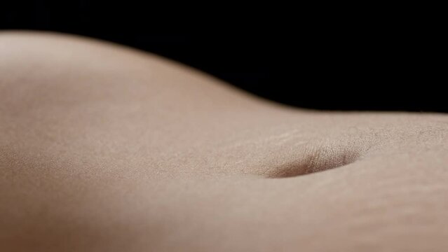 Macro shot of belly of young African American slim female model moving on black background | Skin texture shot for body care concept