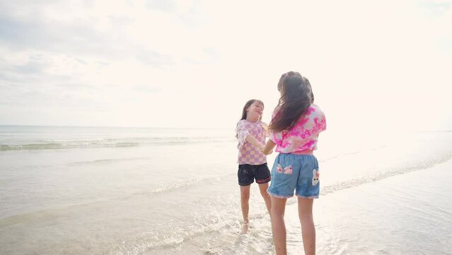 4K Happy Asian family on summer beach vacation. Two little child girl sister playing together on the beach at summer sunset. Children kid sibling enjoy and fun outdoor activity lifestyle at the sea