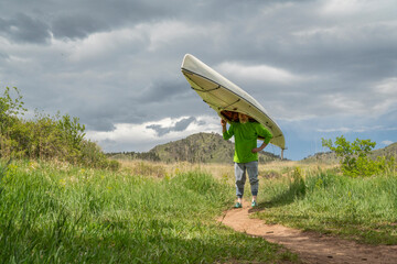 senior male is portaging a decked expedition canoe at foothills of northern Colorado in spring scenery