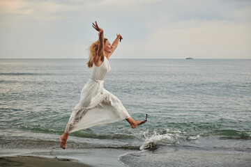 a girl in a white dress jumps on the shore