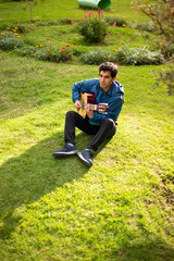 joven cantando y tocando guitarra en un parque al atardecer. Concepto de personas y musica.