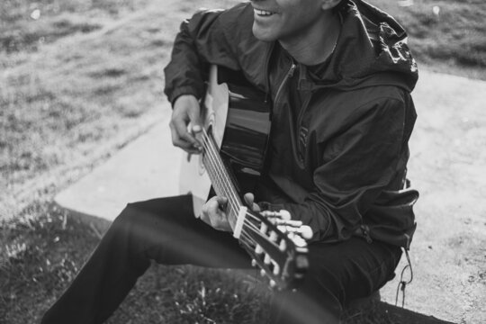 Detalle de joven cantando y tocando guitarra en un parque al atardecer. Concepto de personas y m&uacute;sica.