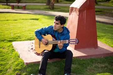 joven cantando y tocando guitarra en un parque al atardecer. Concepto de personas y musica. - obrazy, fototapety, plakaty