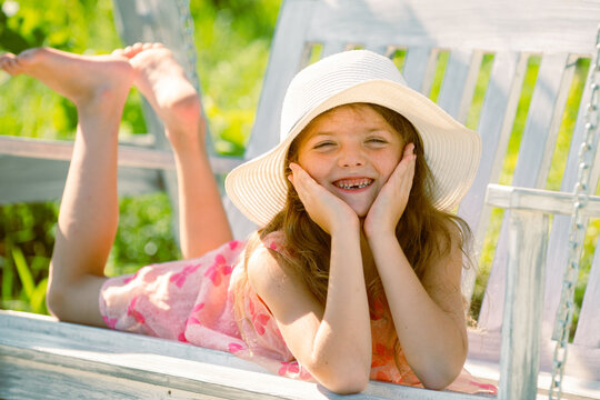 Child swing on backyard. Kid playing oudoor. Happy cute little girl swinging and having fun healthy summer vacation activity. Close up portrait of a beautiful girl in hat dreaming.