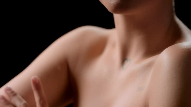 Big close-up shot of good-looking young slim white-skinned woman strokes her shoulders, arms and collarbone turning on black background | Soft skin concept