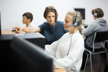 Fourteen-year-old schoolgirl in headphones is engaged in a informatics lesson at a computer