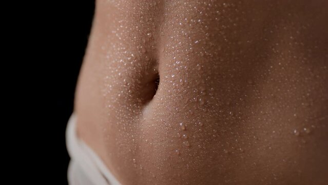 Macro shot of wet good-looking clean flat belly of slim white-skinned female model from different angles on black background | Wet skin texture shot for body hydration concept