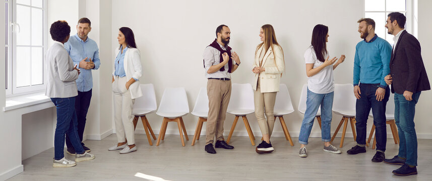 Young people gather for a business meeting in the office. Diverse team of men and women standing and talking in pairs or groups of three at a modern business training event