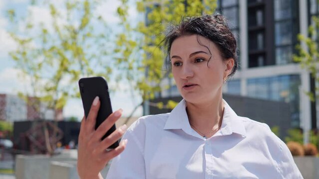 Video Call Portrait of a Beautiful Young Adult Stylish Female Brunette in Smart Formal Clothes Talking to Friends or Colleagues while Standing Outside on City Street. Charming Business Lady Outdoor.