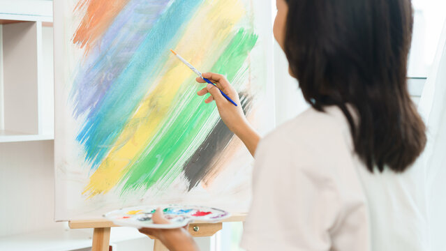 The art concept, Asian female artist using paintbrush to create masterpiece on canvas in art studio