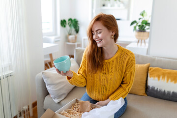 Smiling woman sit on couch at home open post package shopping online buying goods on internet,...