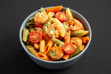 Homemade Tri-Color Penne Salad with Shrimp, Tomato and Basil Bread Crumbs in a Bowl on a black background, side view.