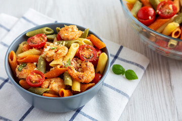 Homemade Tri-Color Penne Salad with Shrimp, Tomato and Basil Bread Crumbs in a Bowl on a white wooden background, side view.