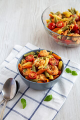 Homemade Tri-Color Penne Salad with Shrimp, Tomato and Basil Bread Crumbs in a Bowl on a white wooden background, side view.
