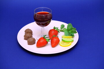 On a plate, a glass of red wine, red strawberries, chocolates, lemon wedges. Red cherry. Romantic...