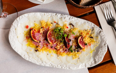 Delicious cod carpaccio with fresh figs and citrus sauce served on white plate. Fish appetizer
