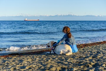 Girl sitting on the beach with her white dog - Esquimalt Lagoon, greater Victoria, British Columbia, Canada 