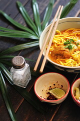 Khao Soi Recipe,Khao Soi,Khao Soi Kai, Thai Noodles Khao Soi, Chicken Curry with seasoning served on black wooden table with decorative leaves, vertical photo.