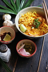 Khao Soi Recipe,Khao Soi,Khao Soi Kai, Thai Noodles Khao Soi, Chicken Curry with seasoning served on black wooden table with decorative leaves, vertical photo.