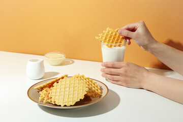 Concept of tasty food with wafers, woman dip a waffle in a glass of milk