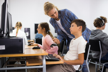 Schoolchildren preparing for lessons in the classroom look at the necessary information on the computer