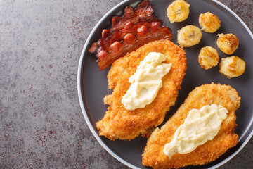 Breaded Chicken Maryland topped with a creamy white gravy served with bananas and bacon close-up in a plate on the table. Horizontal top view from above