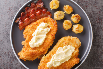 Fried breaded chicken fillet with white sauce served with bananas and bacon close-up on a plate on the table. horizontal top view from above