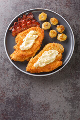 Chicken Maryland is a breaded, pan-fried chicken garnished with bananas and bacon close-up in a plate on the table. Vertical top view from above