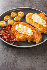 Chicken Maryland is a breaded, pan-fried chicken garnished with bananas and bacon close-up in a plate on the table. Vertical