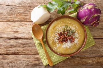 Creamy pureed kohlrabi soup with bacon and parmesan close-up in a bowl on the table. Horizontal top...