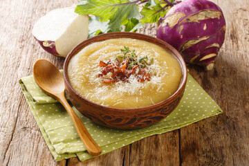 Creamy pureed kohlrabi soup with bacon and parmesan close-up in a bowl on the table. Horizontal