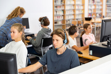 Group of young girls and boys sitting in computer classroom of library and exercising.