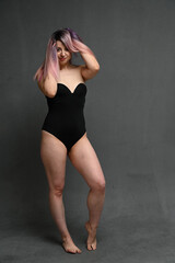 Fototapeta na wymiar Full length adult woman in a black bodysuit holding her hair with a smile