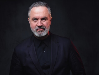 Obraz premium Portrait of handsome elderly dressed in black formal clothes with stylish hairstyle against dark background.