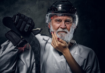 Shot of serious old man hockey player with hockey stick being touched by woman against dark...