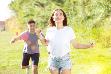 Laughing teenagers playing outdoors funning at grass on summer day