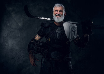 Shot of glad aged hockey player dressed in sportive uniform holding hockey stick.