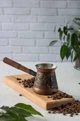 Cezve with coffee on a wooden stand, coffee grains around, ficus in the background.