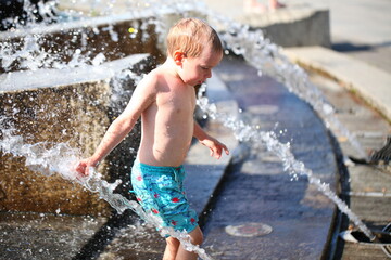 child boy playing in the park in the spray of the fountain