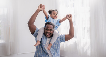 Fototapeta na wymiar Happy black African American father daughter playing at home living room. Afro man carry piggyback little toddler girl. Cheerful family bonding together father’s day concept banner with copy space